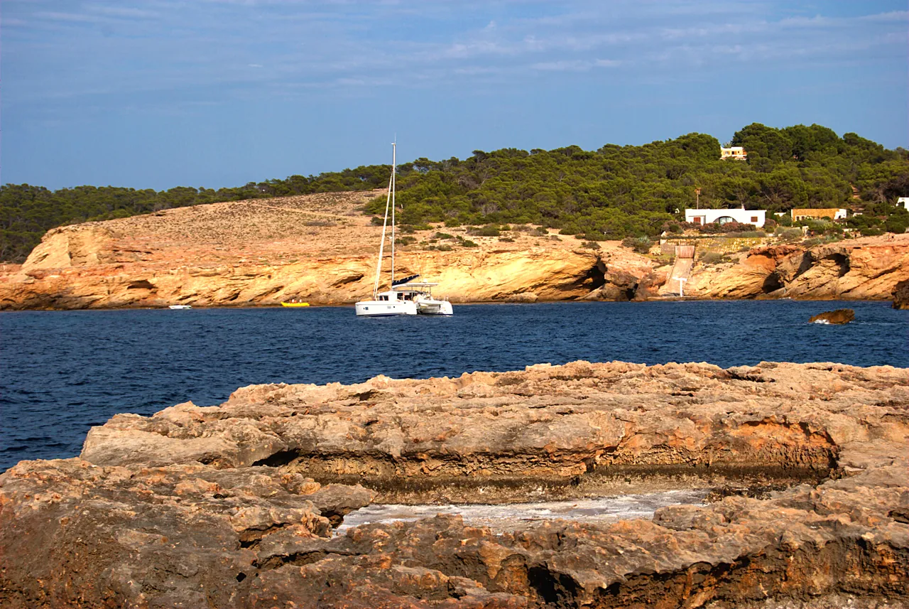 Segelboot vor Anker vor den Felsen und dem Pinienwald von Cala Bassa