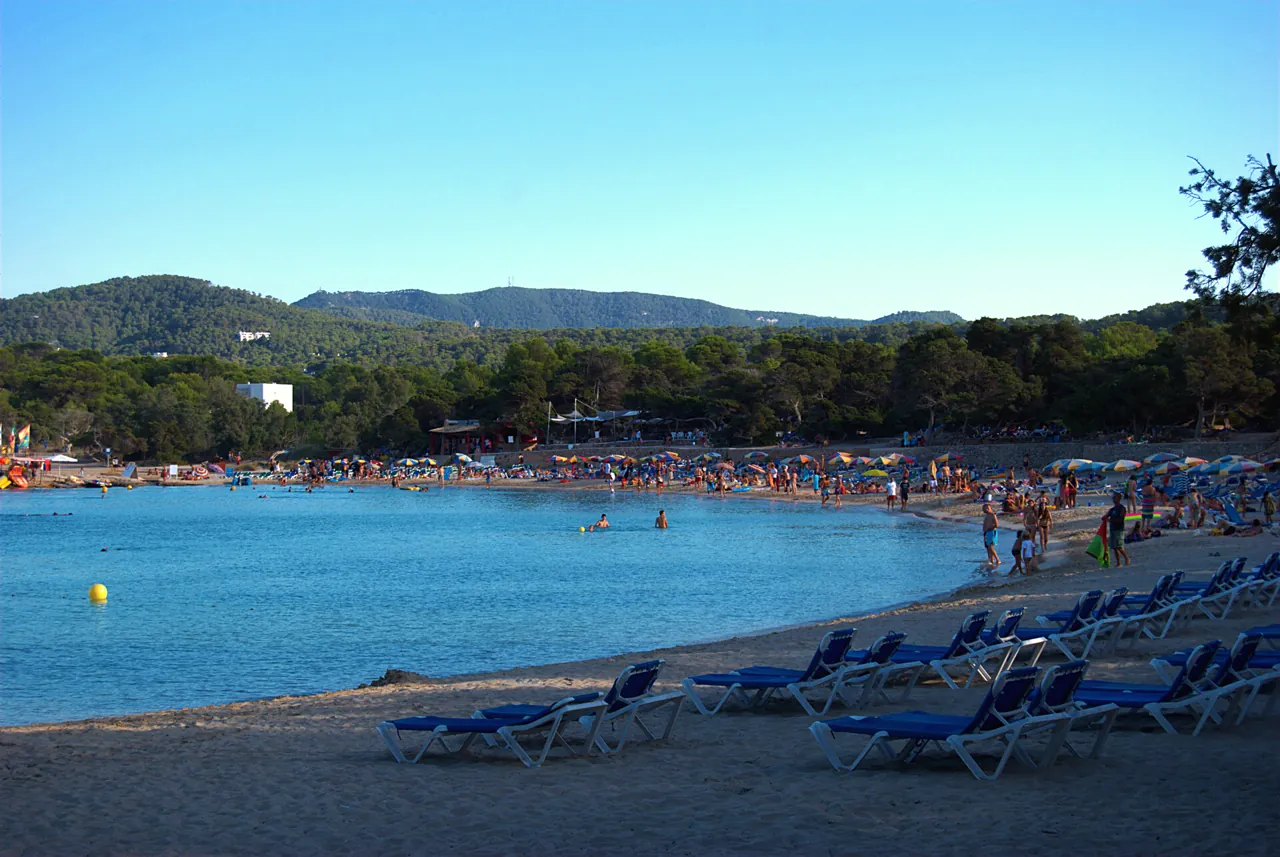 Strand Cala Bassa mit blauen Liegen und Badegästen am Ufer