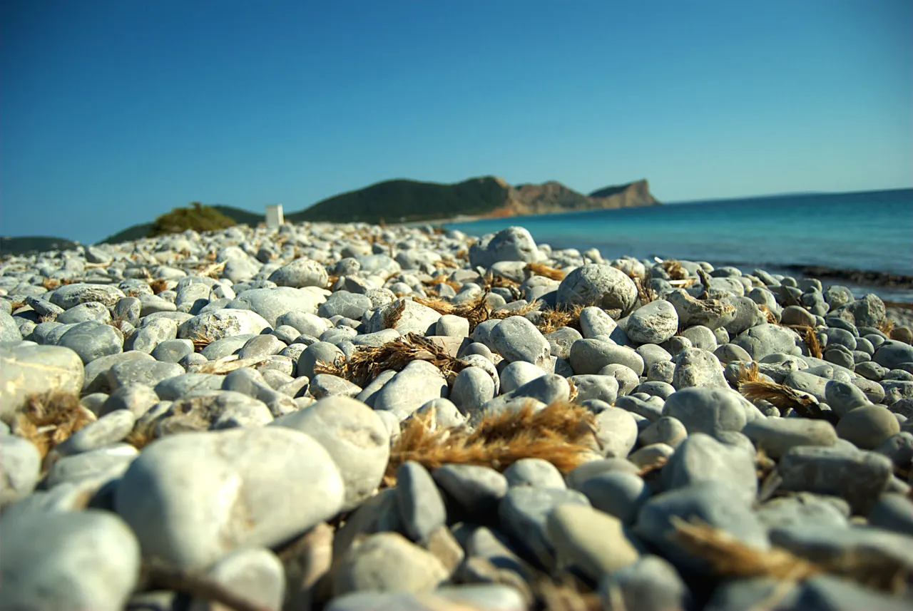 Weiße Steine im Vordergrund mit dem Meer und dem Kap von Es Codolar